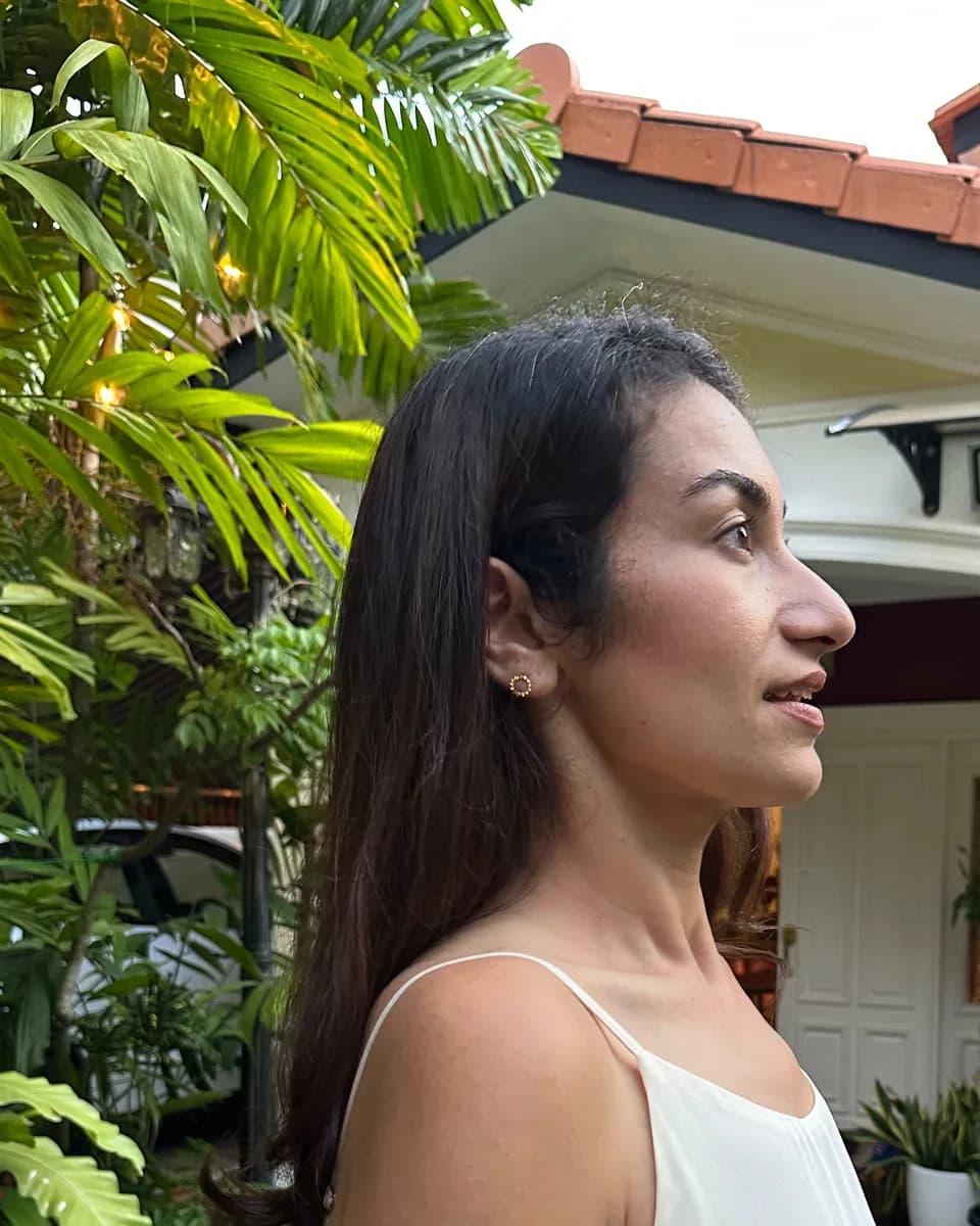 Dr Kavina Shahi in profile in a cream dress, in a garden at dusk, palms and the porch of a house behind her.