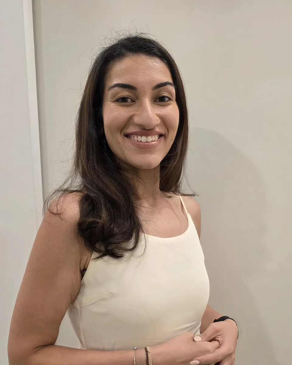 Dr Kavina Shahi in a cream dress smiling at the camera against a plain warm wall.