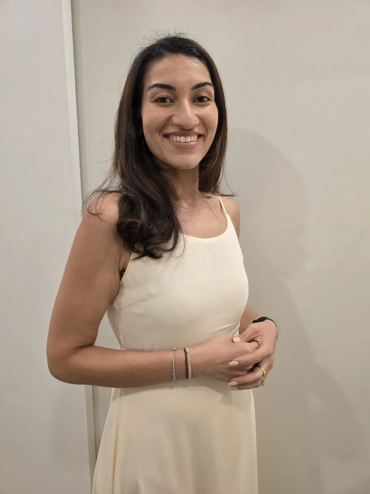 Dr Kavina Shahi smiling at the camera in a cream dress against a plain warm wall.